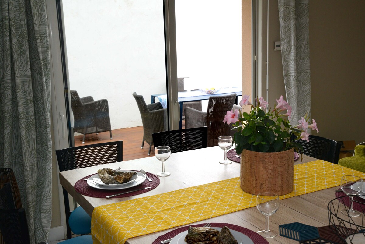 Table à manger dressée avec chemin de table jaune et fleurs, vue sur la terrasse piscine par les portes vitrées — La Maison des Coccinelles