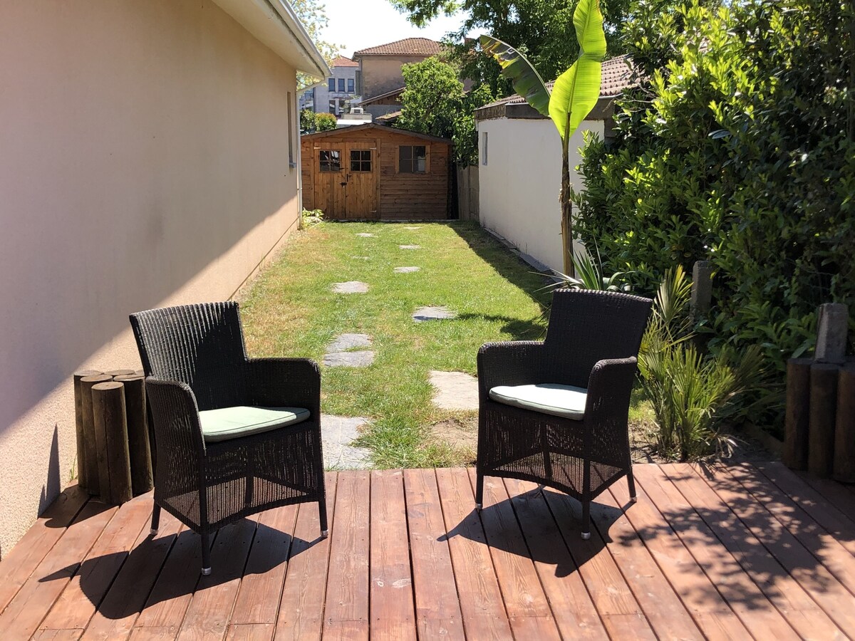 Terrasse en bois avec deux fauteuils en rotin et vue sur le jardin clos — La Maison des Coccinelles