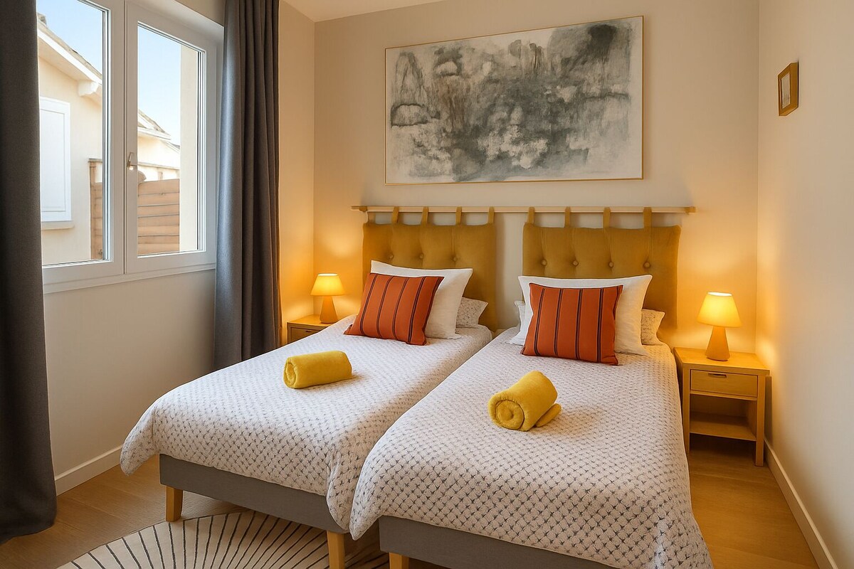 Chambre avec deux lits simples, tête de lit jaune moutarde, coussins rayés orange et serviettes jaunes — La Maison des Coccinelles
