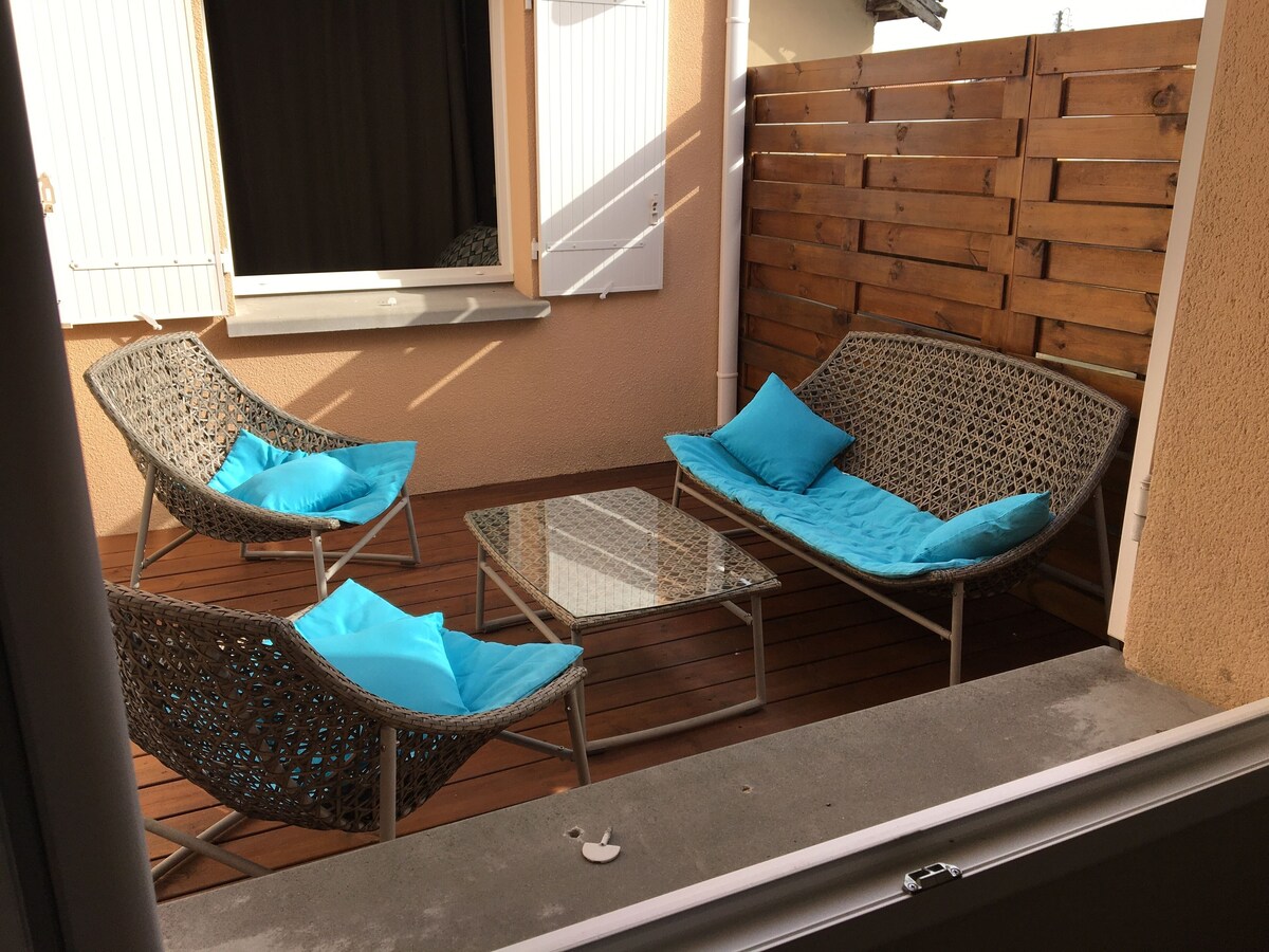 Patio abrité avec fauteuils en rotin et coussins bleus sur terrasse en bois, entouré d'une clôture en bois — La Maison des Coccinelles