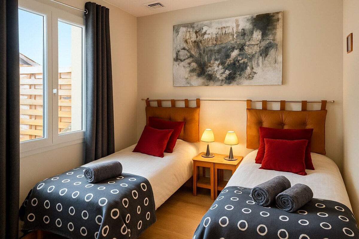 Chambre avec deux lits simples, coussins rouges, lampes de chevet et tableau au-dessus des lits — La Maison des Coccinelles