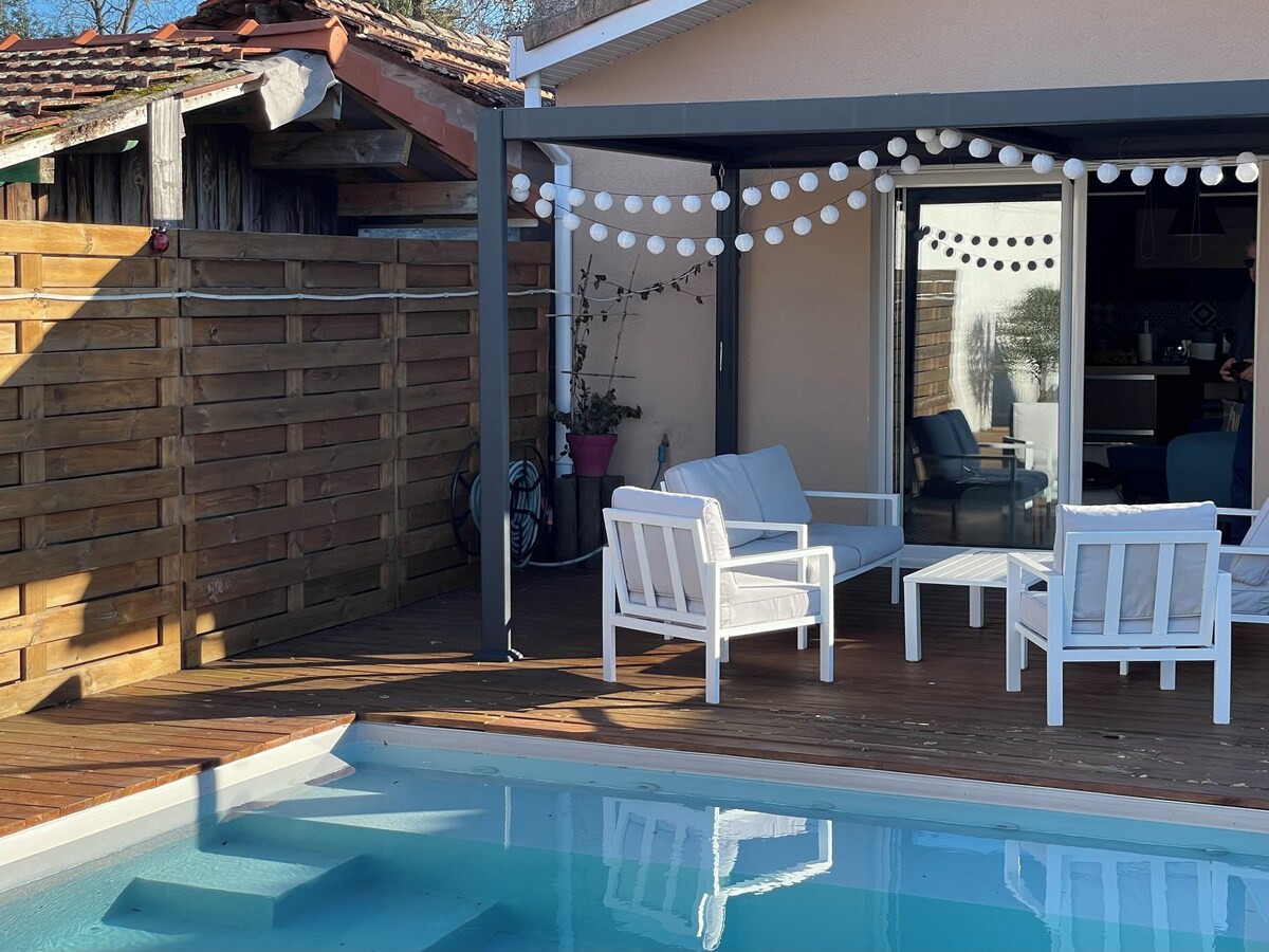 Terrasse piscine avec fauteuils blancs, guirlande lumineuse et pergola en bois — La Maison des Coccinelles