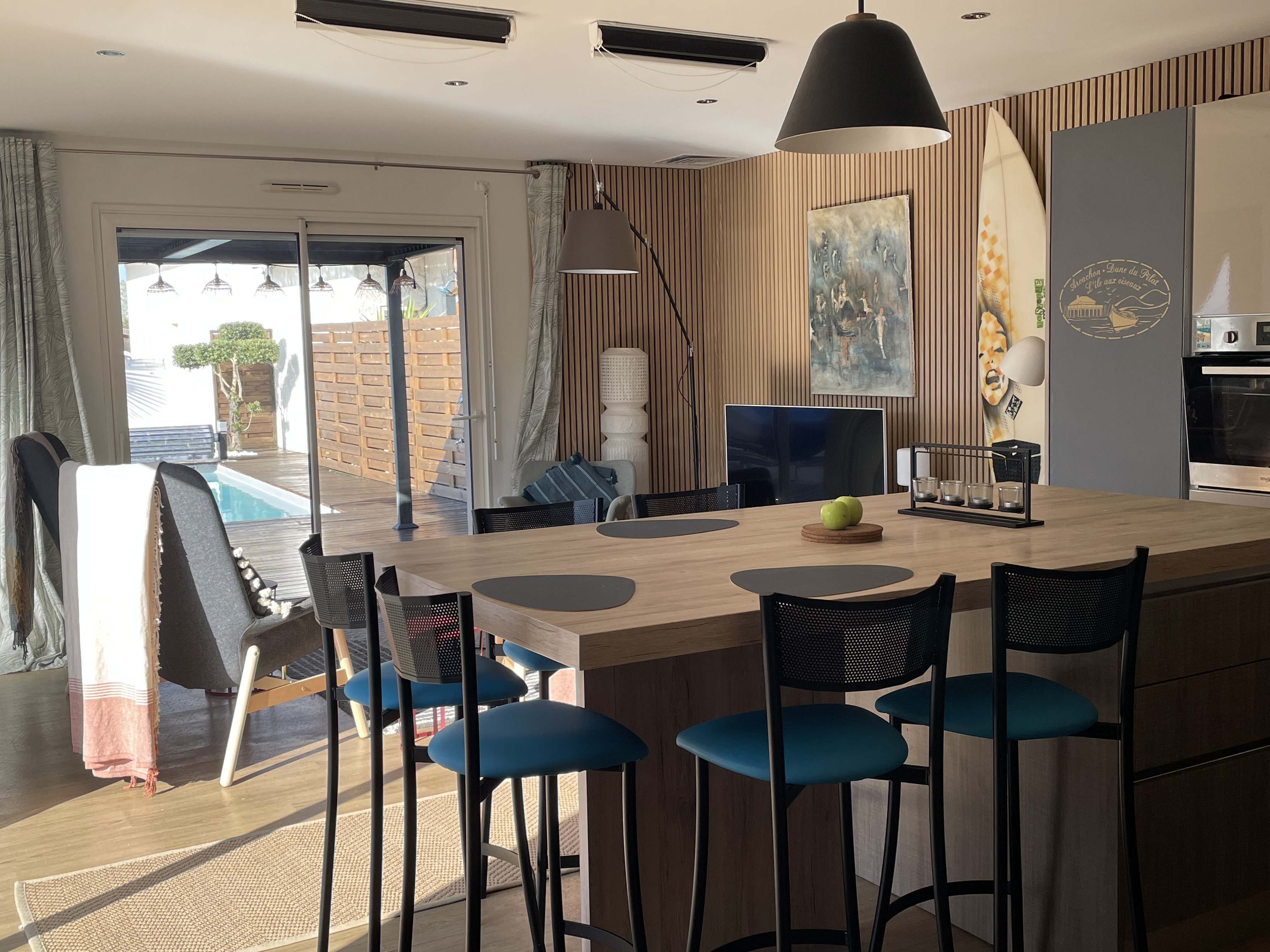 Îlot de cuisine avec tabourets bleus, vue sur le salon et la terrasse piscine — La Maison des Coccinelles