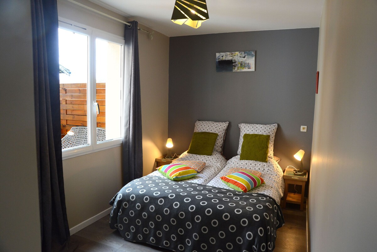 Chambre avec lit double, murs gris, coussins verts et couette à motifs géométriques — La Maison des Coccinelles