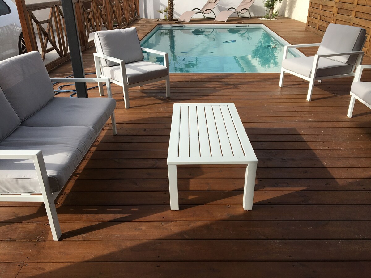 Salon lounge piscine avec canapé blanc, table basse et fauteuil sur terrasse en bois — La Maison des Coccinelles