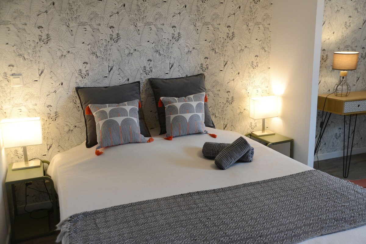 Chambre principale avec grand lit double, papier peint jungle, coussins à pompons orange et lampes de chevet — La Maison des Coccinelles