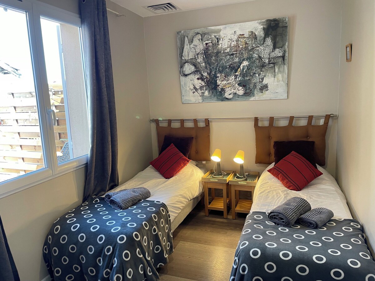 Chambre avec deux lits simples, coussins rouges et lampes de chevet — La Maison des Coccinelles