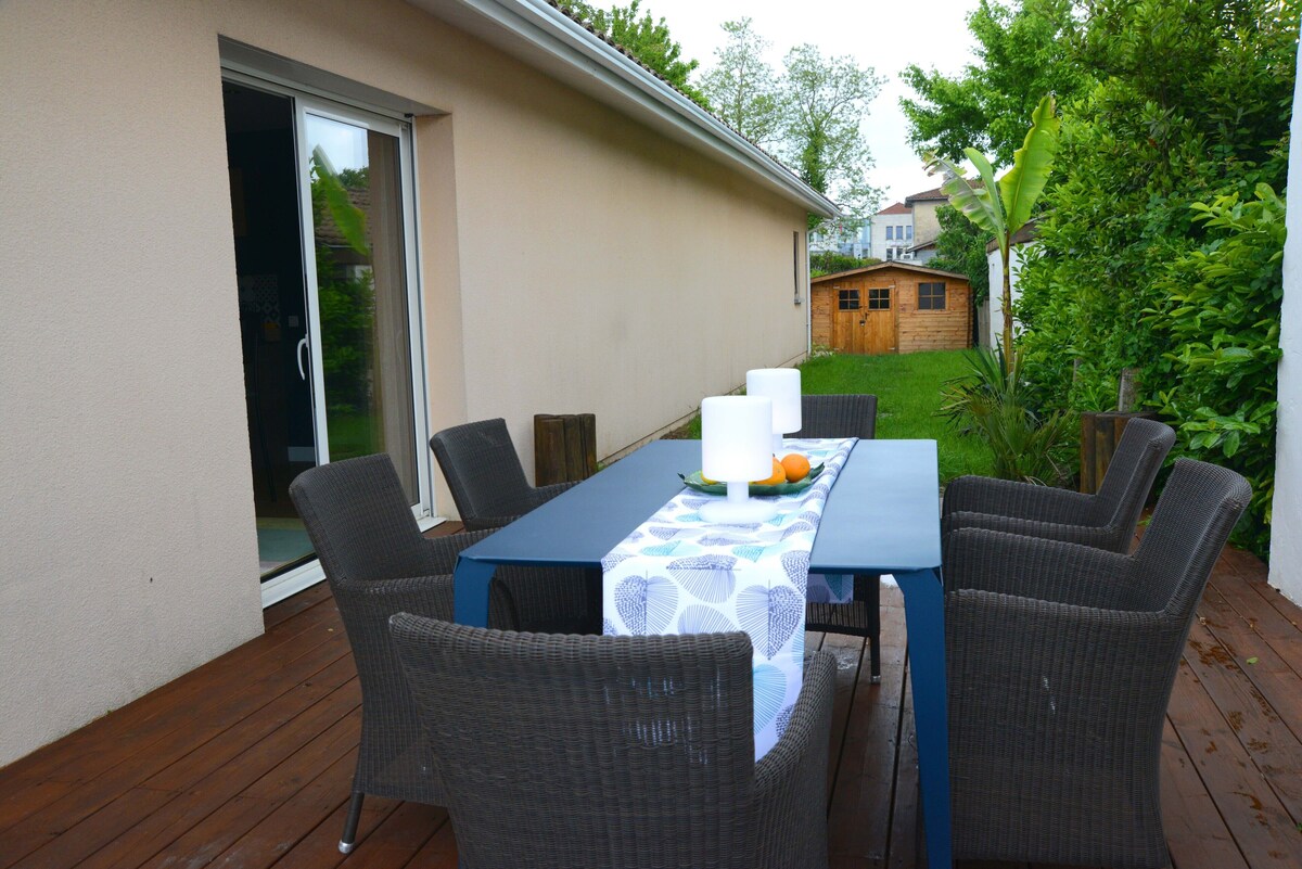 Terrasse repas extérieure avec grande table bleue, chaises en rotin et vue sur le jardin — La Maison des Coccinelles