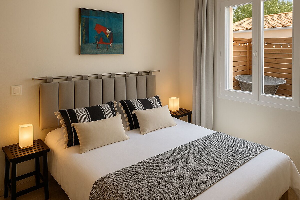 Chambre principale avec grand lit double, tête de lit grise capitonnée et tableau au mur — La Maison des Coccinelles